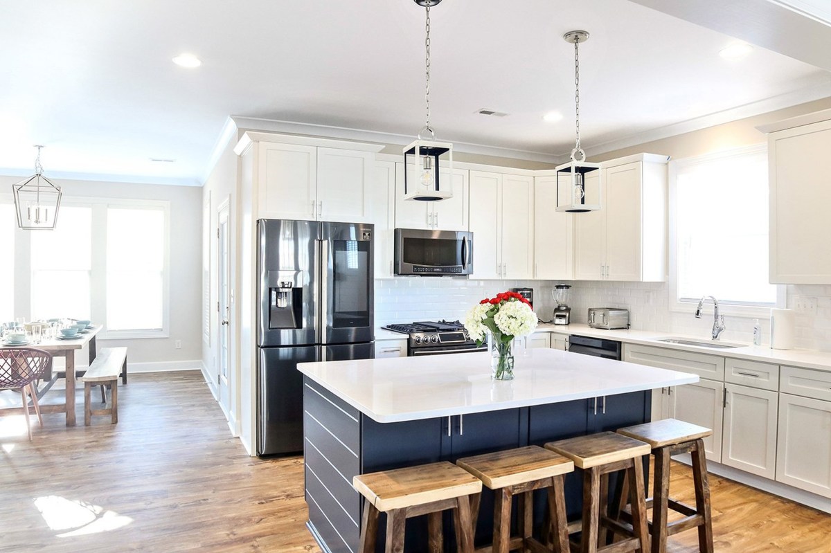An open concept kitchen is shown with a shiplap navy detail island and white shaker cabinets with white quartz countertops. (File photo courtesy of VB Homes)